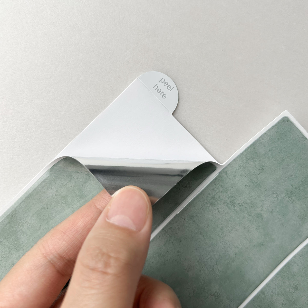 Hand peeling a small adhesive strip from a sheet of jade green tiles