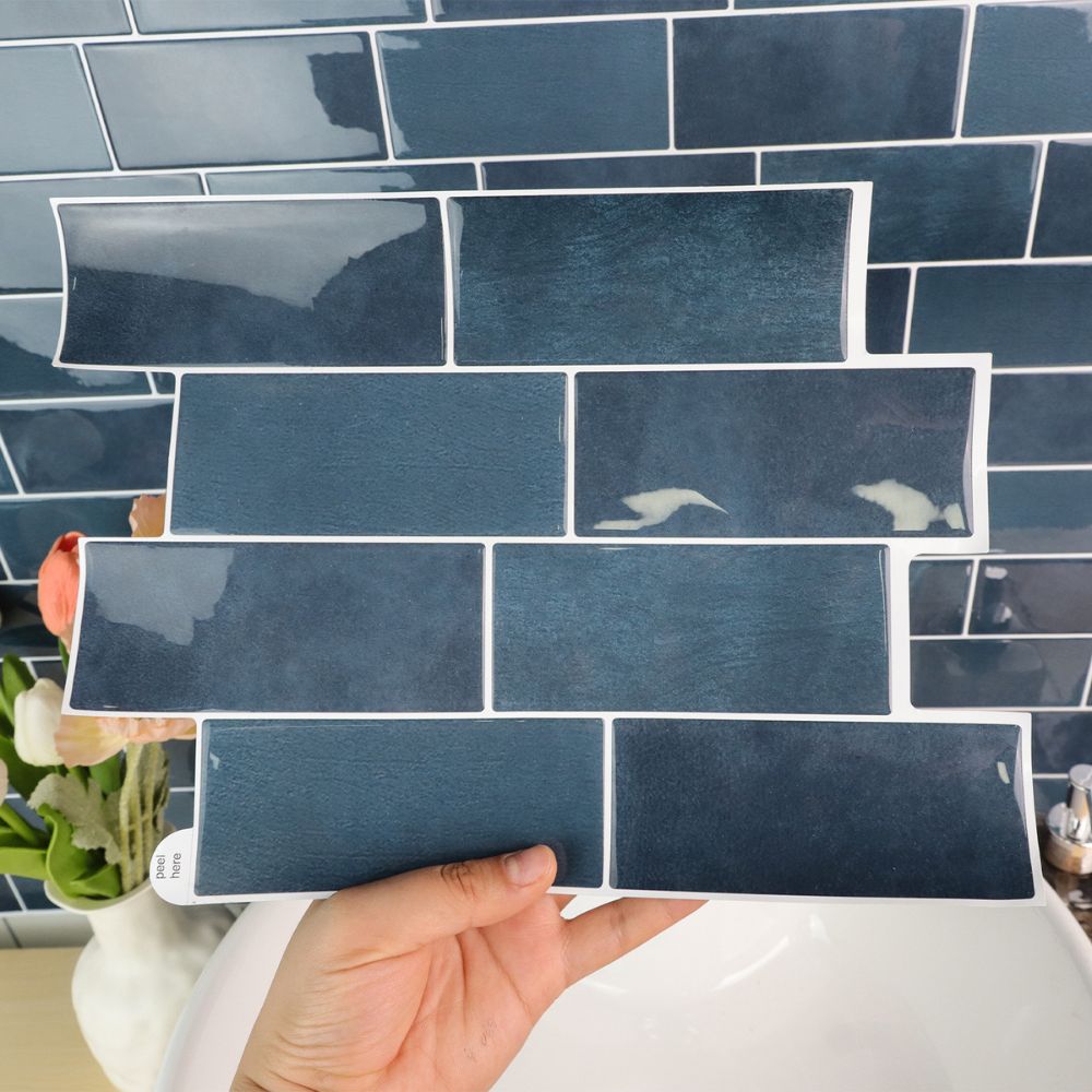 Hand holding a blue tile sample against a tiled wall background