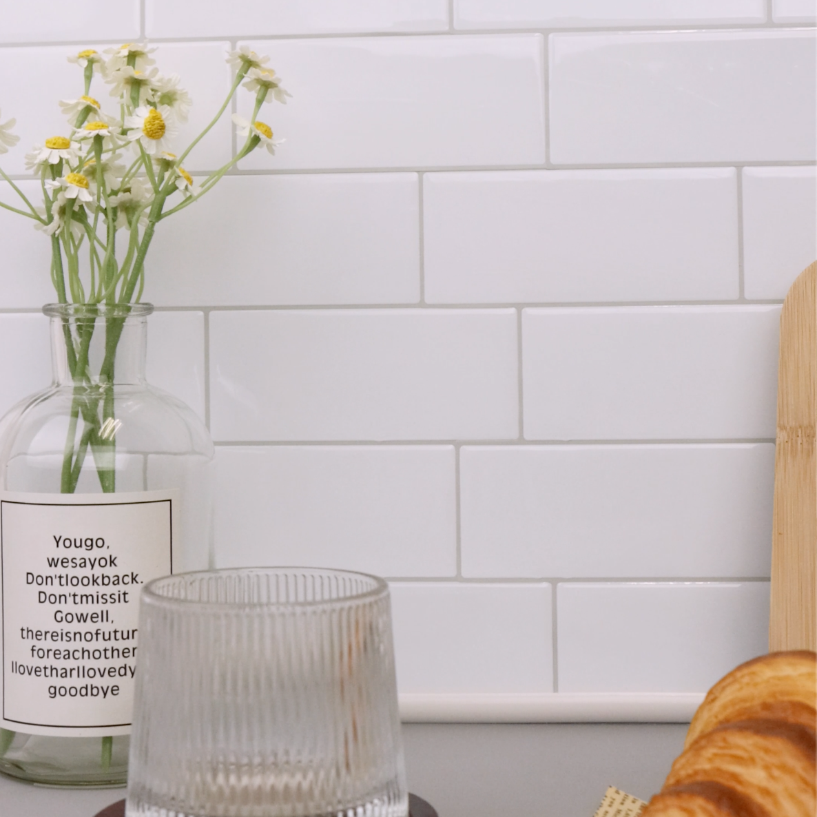 Clear glass vase with flowers on a kitchen counter against a white tiled wall.