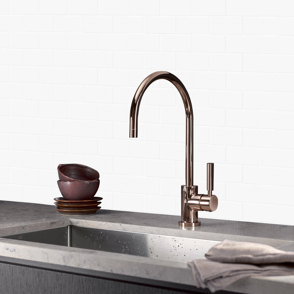 Modern kitchen sink with bronze faucet against a white tiled wall.