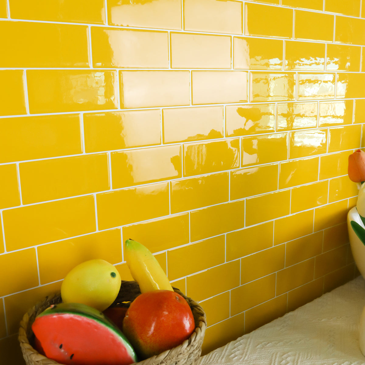 Yellow tiled wall with a basket of fruit and a clown figurine.