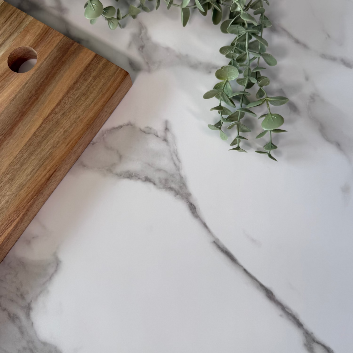 Wooden cutting board on a marble adhesive vinyl with a sprig of greenery.