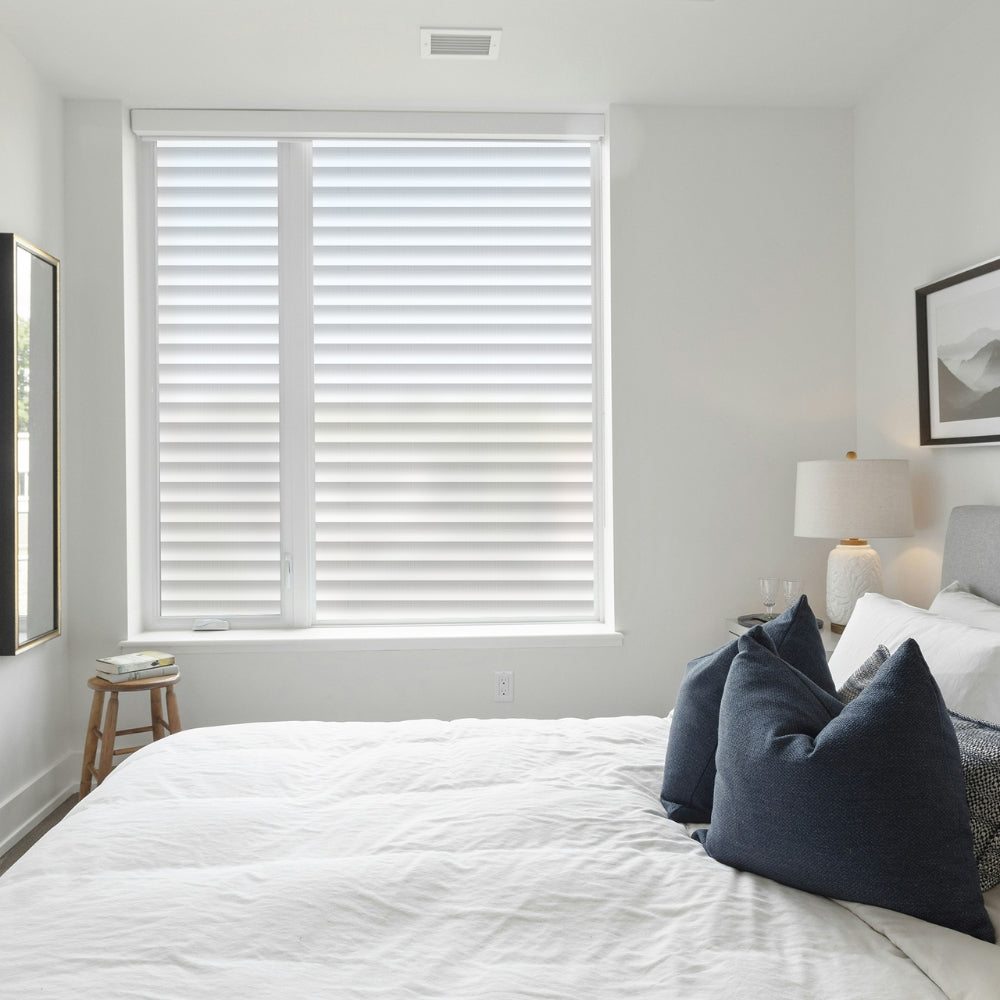 Bedroom with white bedspread, blue pillows, and a window with white venetian blinds window film.