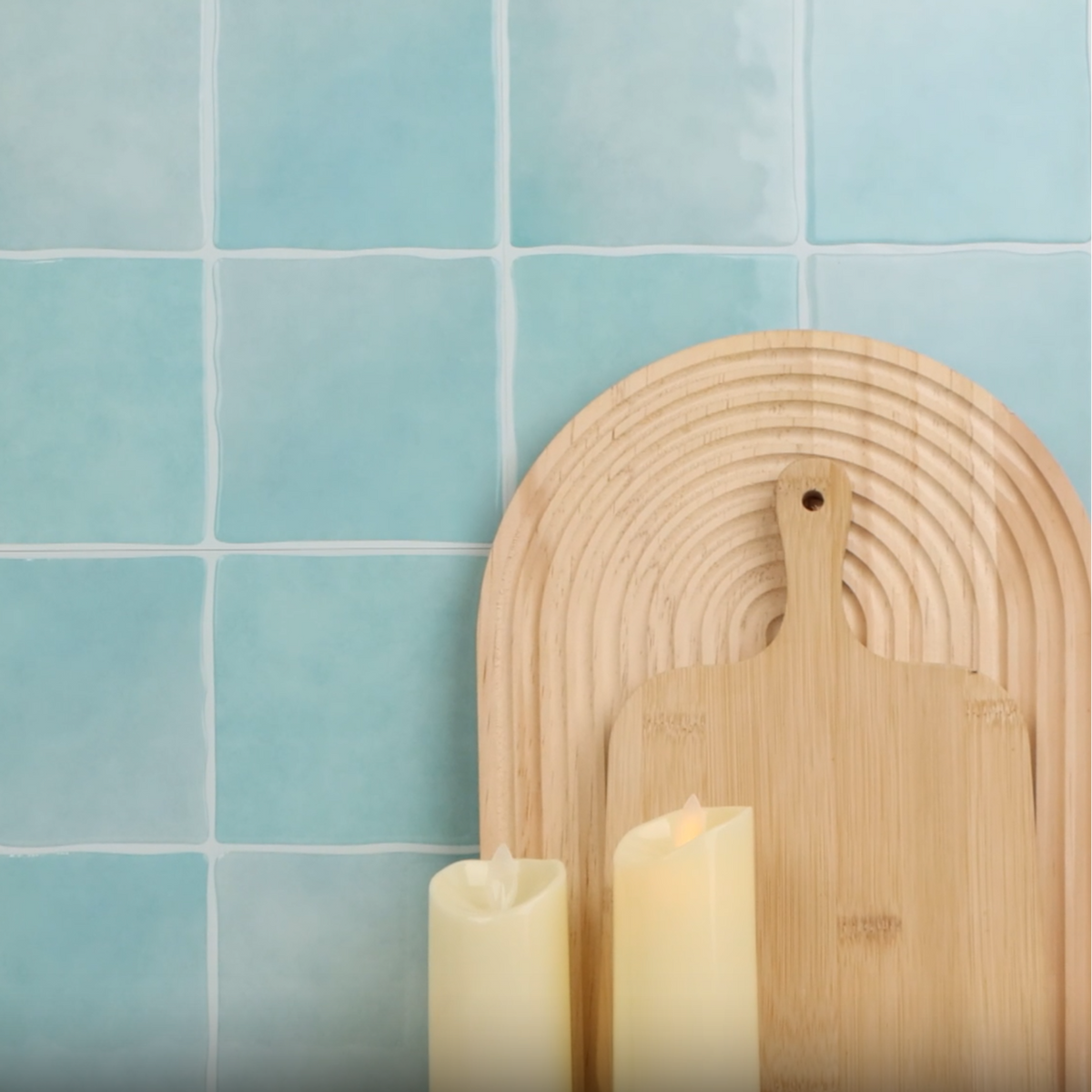Decorative setup with candles, and a wooden cutting board against a blue tiled wall.