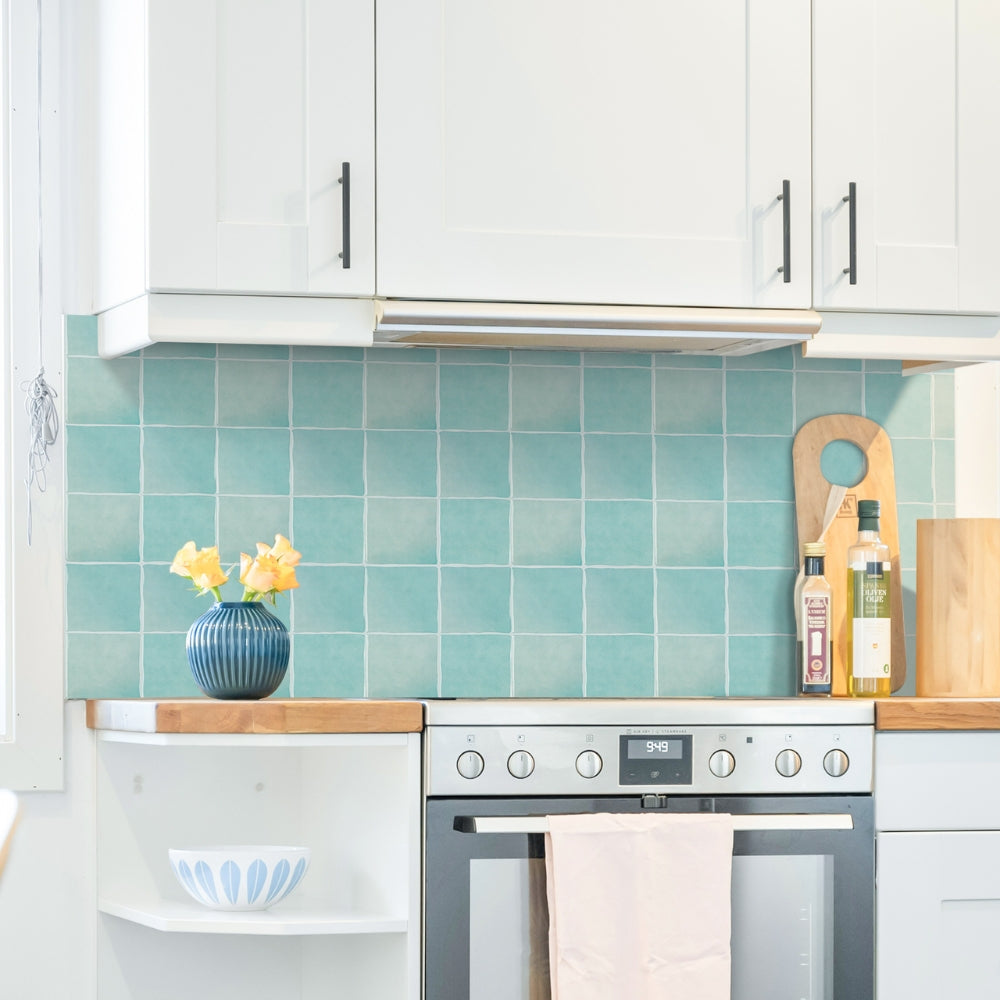 Kitchen with white cabinets, teal tiled backsplash, and wooden countertops.