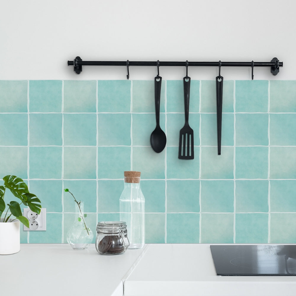 Kitchen with teal tiles, black utensils hanging on a rack, and a white countertop.