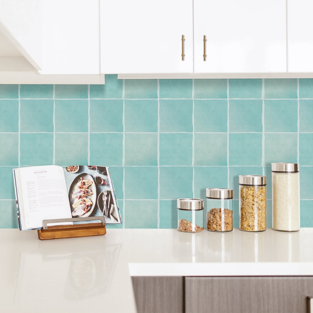 Kitchen counter with turquoise tiled backsplash, jars, and a cookbook.
