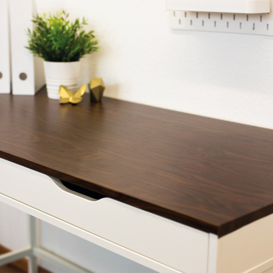 Wooden desk with white drawers and a plant in the background
