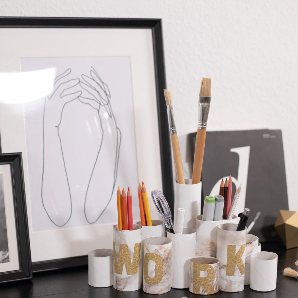 Desk setup with stationery items and framed artwork on a white wall.