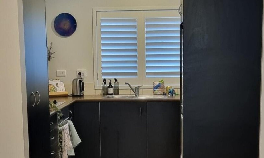 Kitchen with black cabinets, sink, and window blinds.