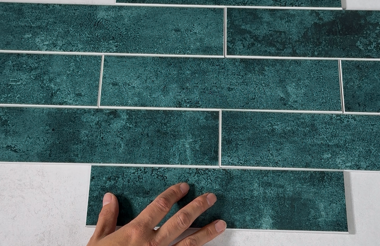 Person touching teal ceramic tiles on a white surface.