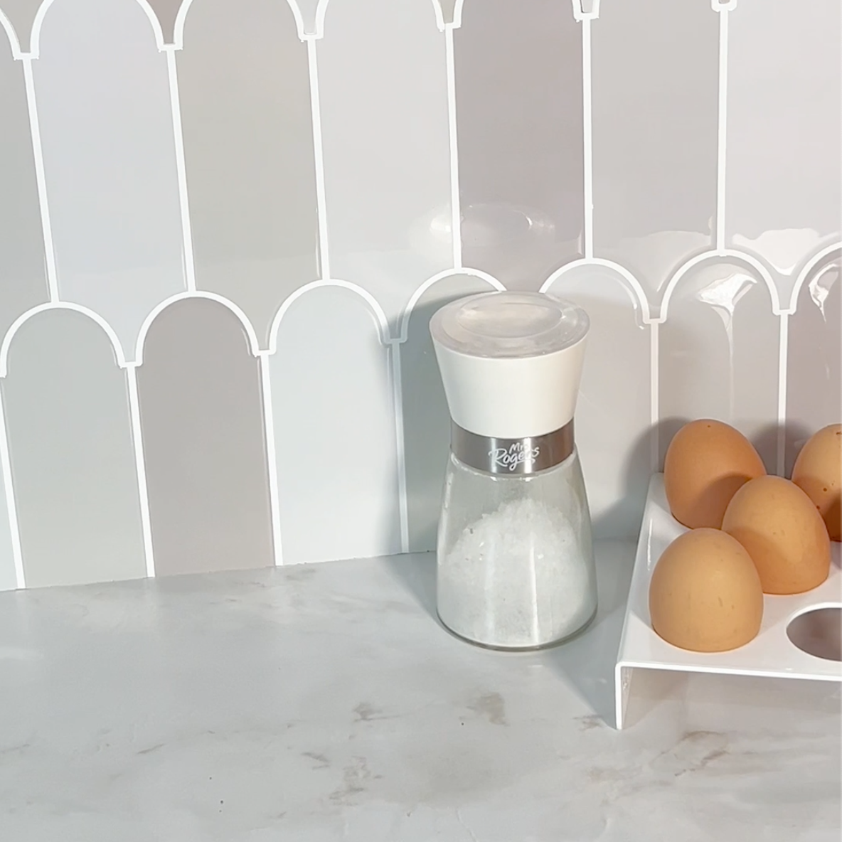 Grey feather tiles backsplash with a salt grinder and eggs on a countertop.
