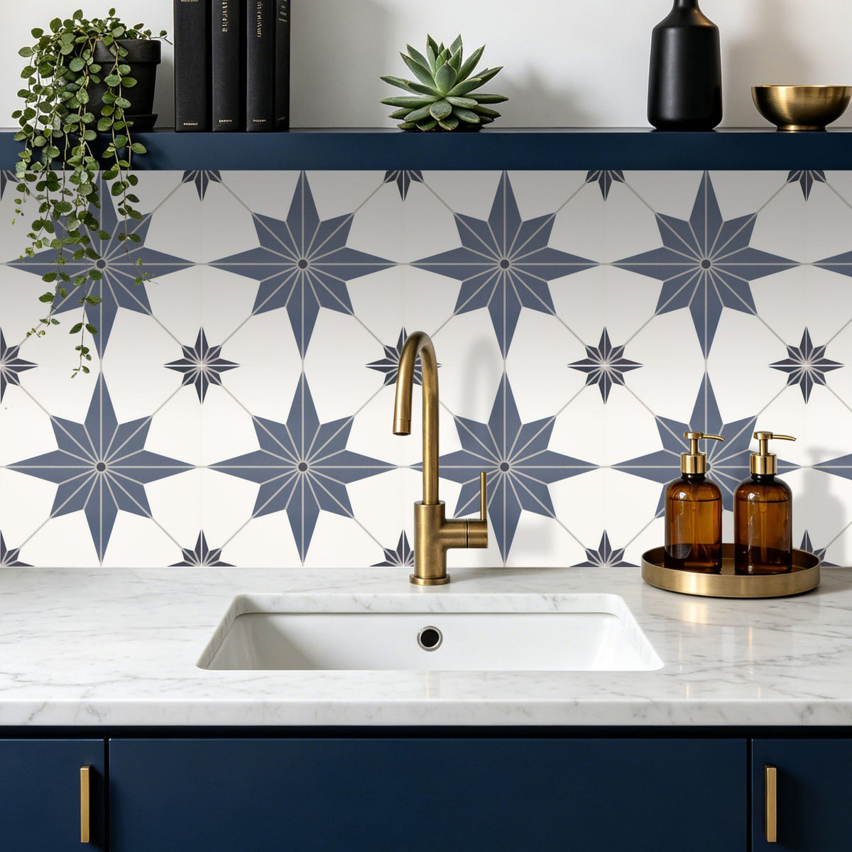A kitchen backsplash featuring white tiles with a blue-grey geometric star pattern, installed behind a white marble sink countertop with a brass faucet.