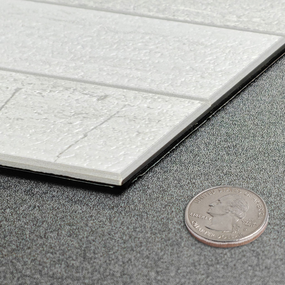A close-up of a textured grey concrete tile sample with a coin placed beside it for scale, showing the tile's thickness and surface detail against a dark grey textured background.