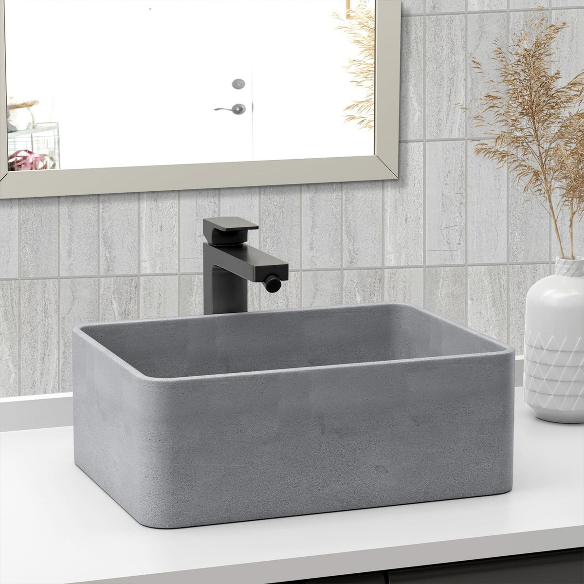 A rectangular grey concrete-look vessel sink with a matte black faucet, set on a white countertop in a bathroom with light grey tiled walls and a mirror.