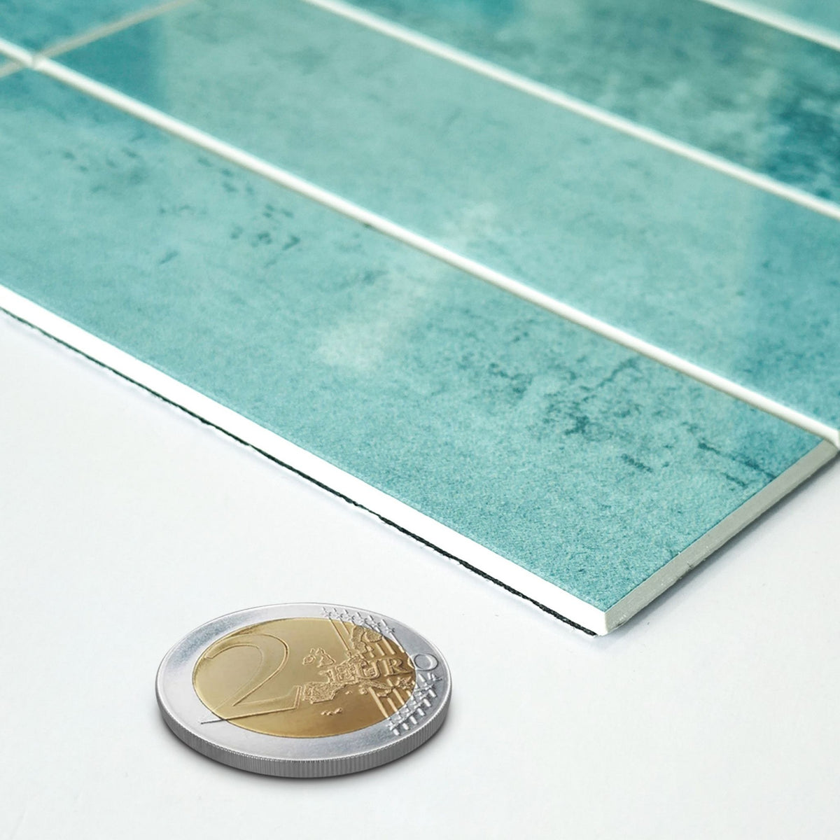 A close-up of glossy rectangular tiles in a mottled teal-green color with white grout lines, shown on a white surface with a 2 Euro coin for scale.