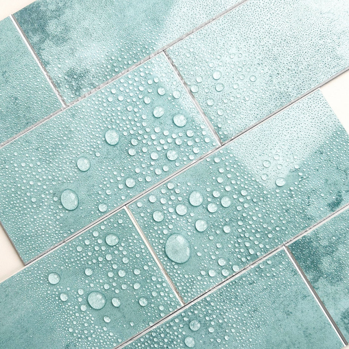 Mint green textured rectangular tiles arranged in a herringbone pattern, covered with water droplets to demonstrate water repellency.