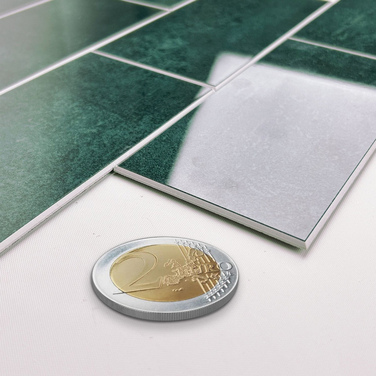 Green glossy rectangular wall tiles with white grout lines, shown in a close-up with a 2 Euro coin for scale on a white surface.