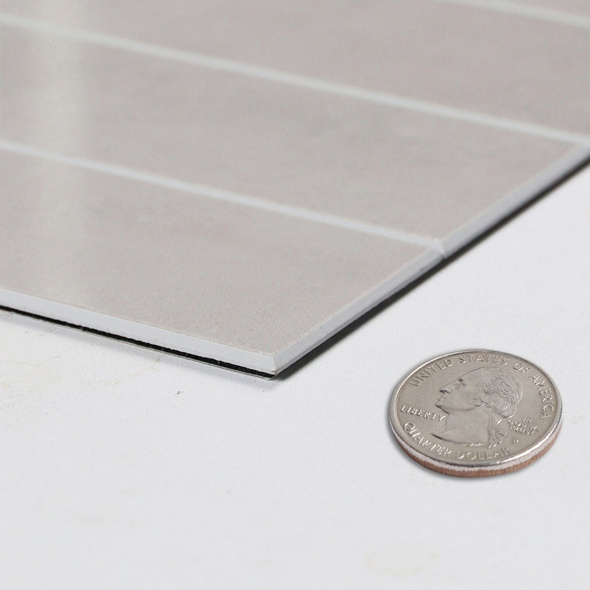 A close-up of a light pink rectangular panel with a brushed metallic finish, shown on a white surface next to a U.S. coin