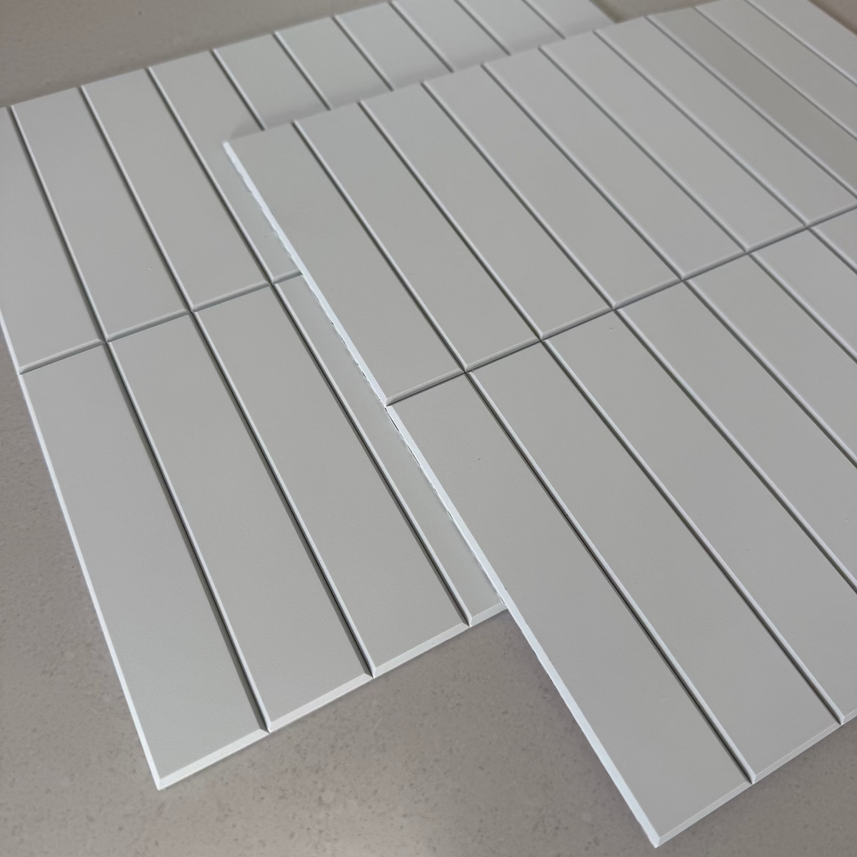 Two sheets of white matte kit kat tiles, arranged on a light grey surface.